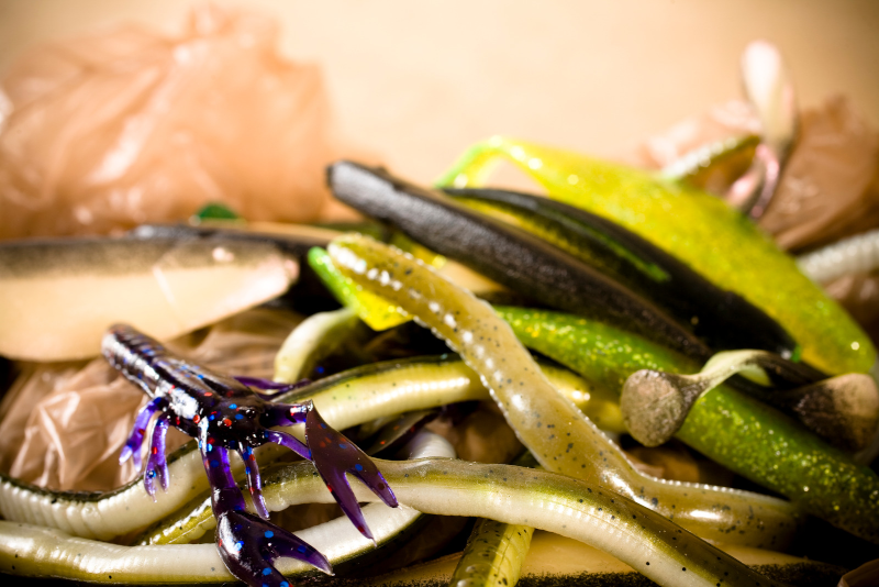 A pile of soft plastic fishing baits used for bass fishing with a purple crawfish in focus